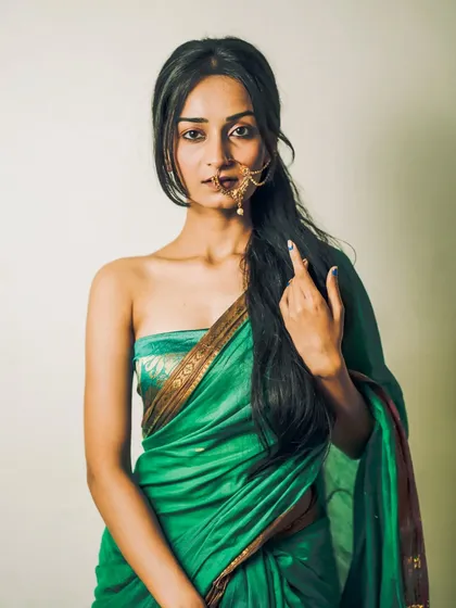 A modern take on a traditional look, this portrait features a model in a strapless green saree, showcasing her long hair and elegant nath.