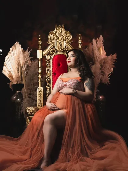 Feel like the queen you are in our Maharaja royal chair setup. This mom-to-be looks powerful and majestic, seated on a golden throne in a dramatic, low-light setting.