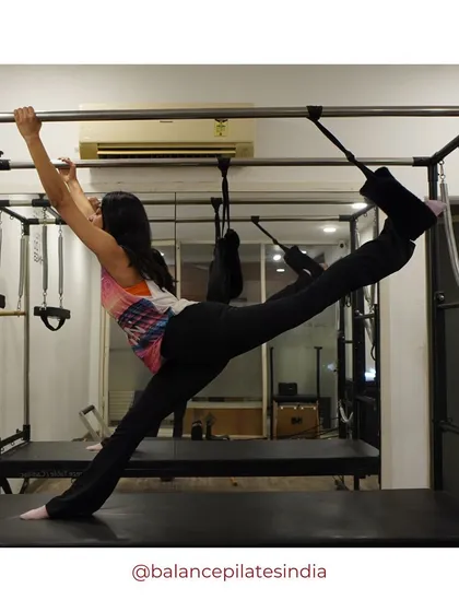 A client demonstrates incredible flexibility and strength on the Cadillac/Trapeze Table. This advanced equipment allows for a huge range of challenging exercises.