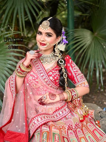 A full view of a model looking stunning in a red and pink lehenga, surrounded by lush greenery. This shows how vibrant our outfits look in outdoor photoshoots.