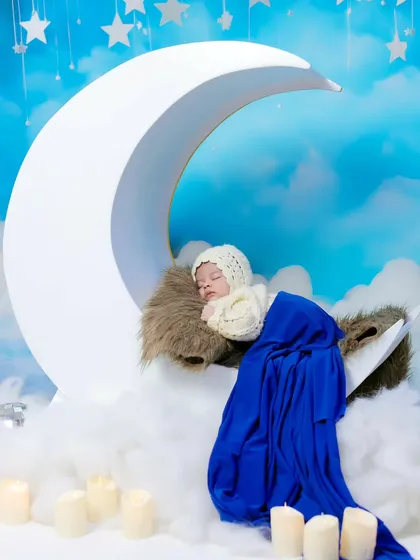 A beautiful, serene shot of a newborn sleeping on a large moon prop, set against a dreamy sky backdrop. Our studio is filled with props to create magical scenes.
