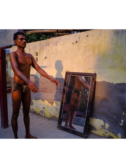 A wrestler stands proudly, his shadow cast on the wall behind him. This image captures the strength and physique of the athlete in the warm evening light.