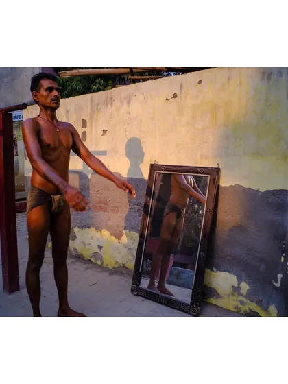 A wrestler stands proudly, his shadow cast on the wall behind him. This image captures the strength and physique of the athlete in the warm evening light.