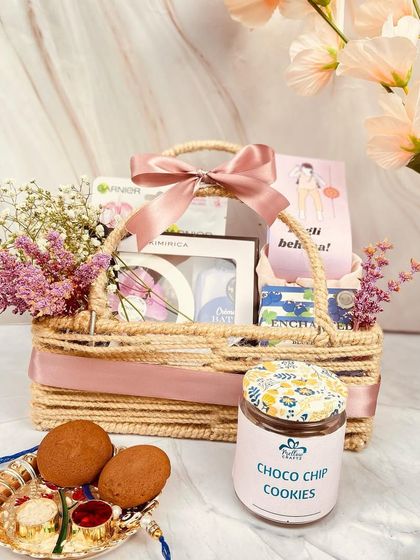 A charming mini basket hamper for a sister, featuring a jute basket, fresh flowers, choco chip cookies, and other pampering items.