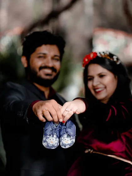 A classic announcement-style photo where the couple holds up a tiny pair of baby shoes. It's a sweet and personal way to share the excitement of their coming arrival.