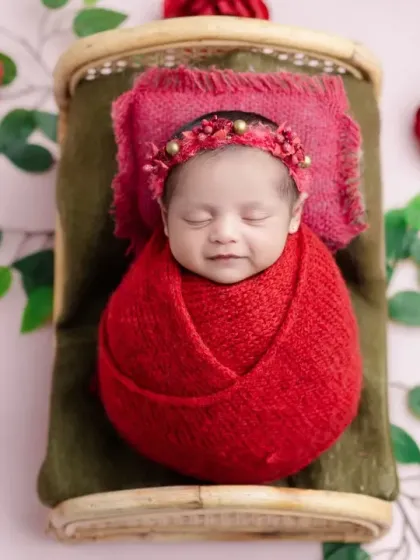 A smiling newborn in our red rose setup, looking cozy and content.