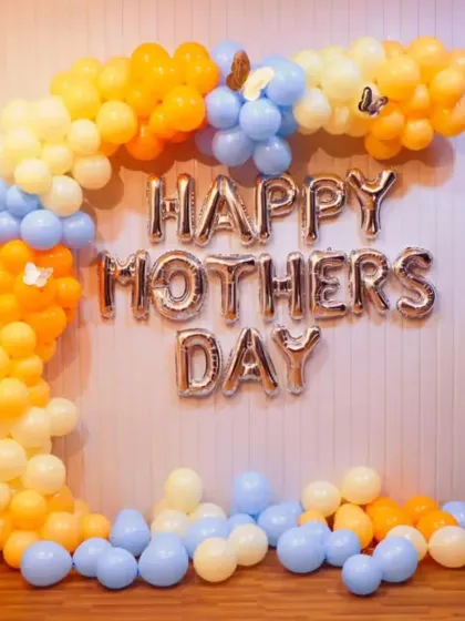 A colorful 'Happy Mother's Day' decoration with a pastel blue, yellow, and orange balloon arch.