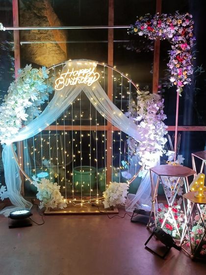 A gorgeous 40th birthday decoration with a rustic, romantic feel, using a circular frame with fairy lights, sheer drapes, and floral arrangements.