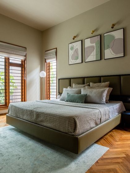 In another bedroom, we used a soothing olive green palette paired with herringbone wood flooring. Large slatted windows allow for ample natural light while ensuring privacy, and abstract art adds a touch of modern personality.