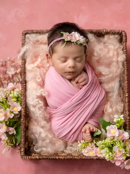 A classic newborn pose, this baby is swaddled snugly in pink and nestled in a basket surrounded by cherry blossoms.