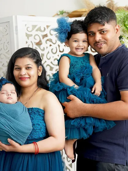A beautiful family of four dressed in coordinating shades of blue. The mother holds her newborn while the father holds their smiling toddler, capturing a perfect family moment.