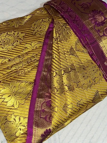 A gold and purple brocade saree, folded to showcase its luxurious pattern.