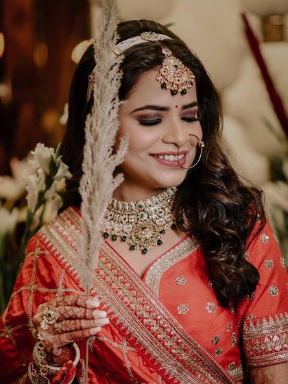 A lovely bridal portrait where the bride is holding a piece of pampas grass. The soft, bohemian element contrasts beautifully with her traditional orange lehenga.