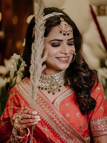 A lovely bridal portrait where the bride is holding a piece of pampas grass. The soft, bohemian element contrasts beautifully with her traditional orange lehenga.