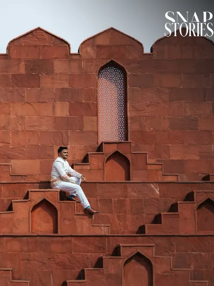 A powerful solo portrait of the groom against the dramatic backdrop of a red sandstone fort, showcasing a modern and stylish approach to groom photography.