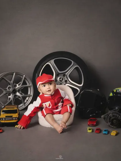 A full view of the 'Biker Baby' setup, featuring a baby boy in a red racing suit surrounded by real car parts, wheels, and toy cars. This is a great example of a highly customized themed session.
