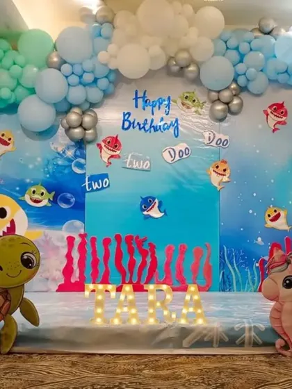 A fun-filled "Baby Shark" second birthday party. The underwater theme is complete with character cutouts, a coral reef backdrop, and a blue and green balloon arch that looks like ocean waves.