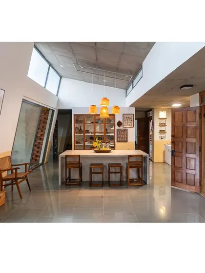 The heart of the 'Aamra' farmhouse, where the dining area flows into the living space. The custom concrete island, wooden bar stools, and upcycled pantry cabinet are all designed to foster connection, blurring the lines between cooking, eating, and living.