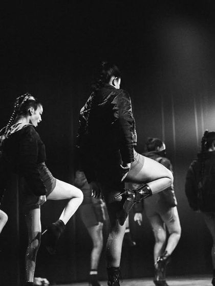 A dramatic black and white photo capturing the powerful silhouettes of our Heels dancers on stage.