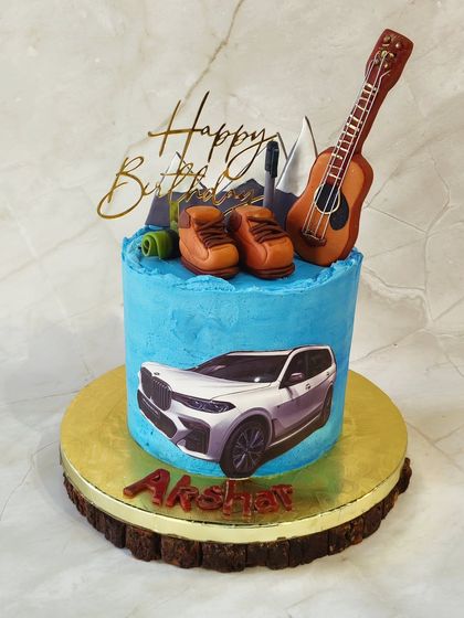 A cake that captures all of someone's passions. This design features an edible print of a BMW, along with fondant hiking boots, a guitar, and mountain toppers to represent a love for cars, music, and adventure.