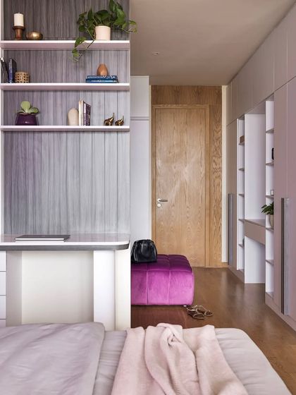 The walk-in closet in the master bedroom is anchored by a cozy purple pouffe, connecting it to the main bedroom's color scheme. The fluted glass sliding doors add a touch of elegance.