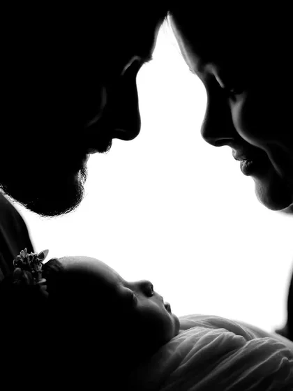 An artistic black and white silhouette of parents gazing down at their newborn. This high-contrast, intimate shot emphasizes emotion and connection, offering a timeless and classic portrait style.