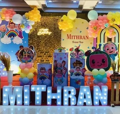 A vibrant Cocomelon party with a gold sequin backdrop and large marquee letters. The setup is filled with character cutouts and colorful balloon arrangements.