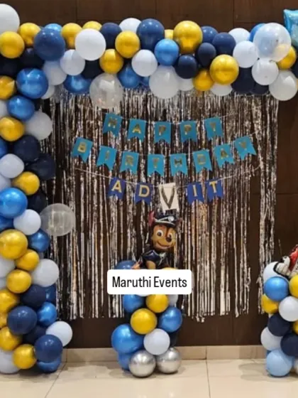 A Paw Patrol theme in a classic blue, gold, and white color scheme. The balloon arch frames a silver foil curtain, with character cutouts on the balloon columns.