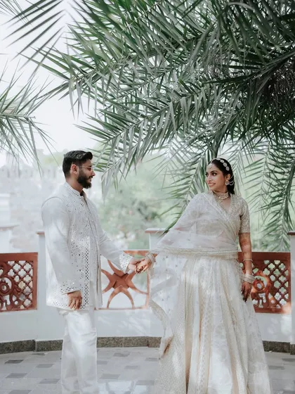 A beautiful moment shared between the couple under the shade of palm trees. Their coordinated white outfits stand out against the rustic terracotta details of the fort architecture.