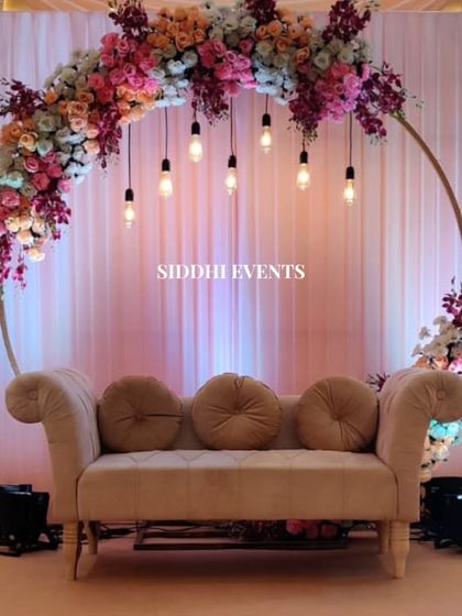 A semi-circular floral arch with hanging bulbs creates a modern and romantic frame for this elegant reception seating area. The mix of colorful flowers adds a touch of vibrancy.