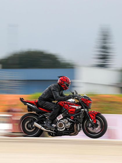 A red and black custom sportbike speeds down the track, its unique design standing out.