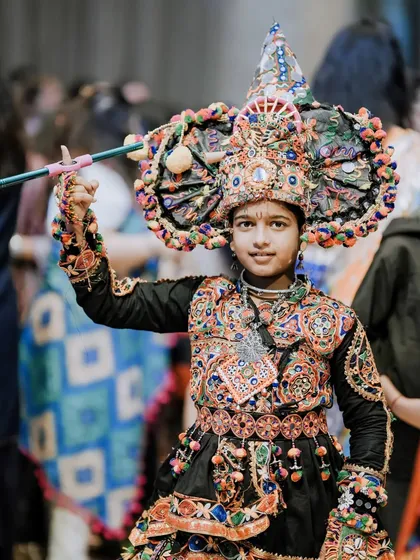 A young boy in an elaborate, prize-worthy Navratri costume, posing confidently with his dandiya stick.