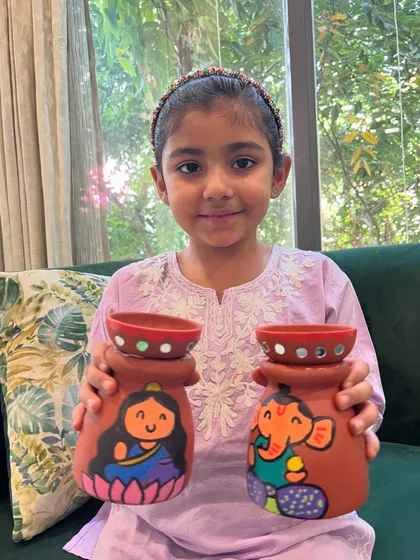 This student is showing off her hand-painted Lakshmi and Ganesha tea-light holders, perfect for lighting up her home during Diwali.