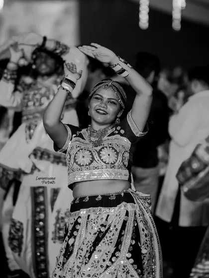 A black and white shot of a woman dancing, her hands raised in a classic Garba pose, her happiness evident.