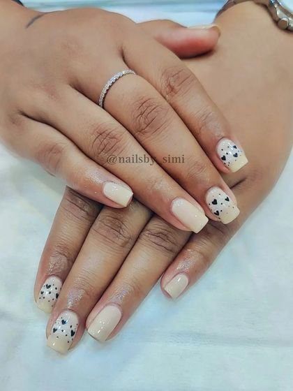 A nude base gel polish with small, freehand black hearts on the accent nails.