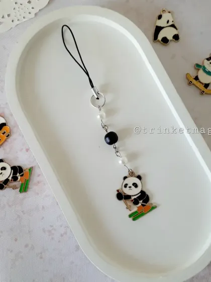 This panda charm is perfect for adding a cute touch to your phone or keys. It's a simple, handmade piece featuring a skiing panda with black and pearl beads.