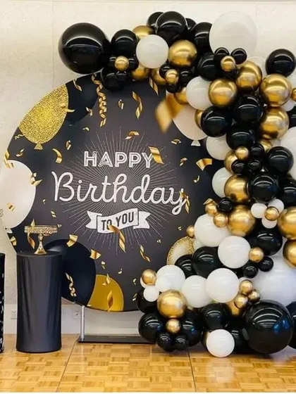 An elegant birthday backdrop with a custom printed circular panel and a balloon garland in black, white, and gold.