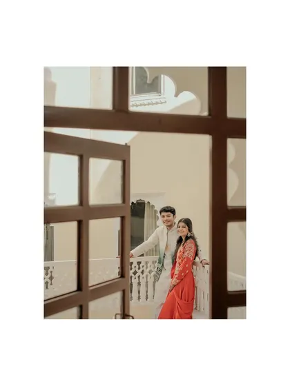 A creatively framed shot of the couple on a palace balcony, viewed through a window. This adds depth and an intimate, "stolen moment" feel to their destination pre-wedding photo.