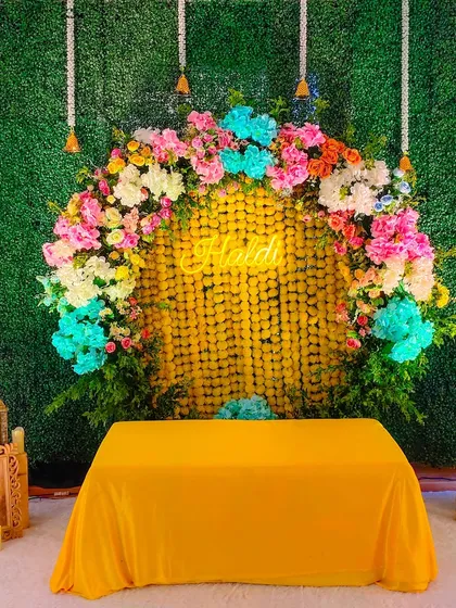 For a modern twist on Haldi decor, I created this backdrop using a green grass wall, a curtain of marigolds, and a vibrant multi-colored floral arch.