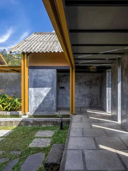 A play of light and shadow along the exterior corridor of Teyla, where yellow steel columns contrast with grey concrete walls and a corrugated roof.