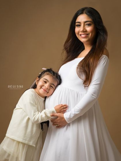 A daughter's sweet hug for her expectant mother. This portrait, set against a warm, neutral backdrop, is full of love and tenderness.