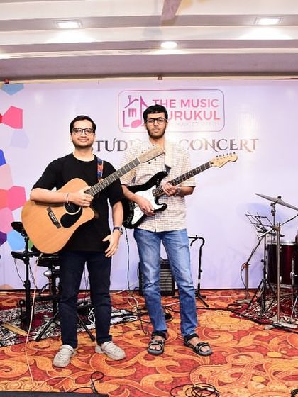 Two of our adult guitar students, one on acoustic and one on electric, stand proudly on stage after their performance. It shows the range of styles and the camaraderie among our students.