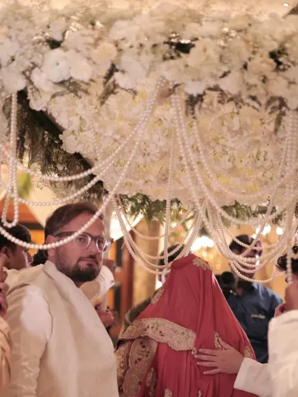 A close-up of the bride's entrance under the floral and pearl chaadar, a moment of tradition and beauty.