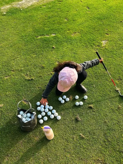 A young golfer gathers her practice balls, ready to put in the work on the chipping green.