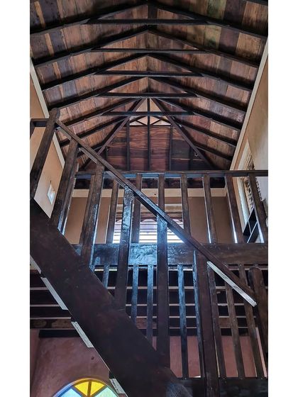 A view up into the 'atta' or attic space of the Doddaballapura mud house. The entire structure, from the railings to the roof trusses, is crafted from reclaimed wood, showcasing its beauty and strength.