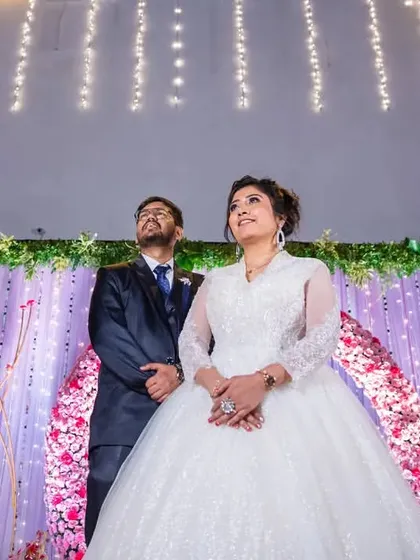 A grand, wide shot of the couple on their beautifully decorated reception stage, looking up at the lights.