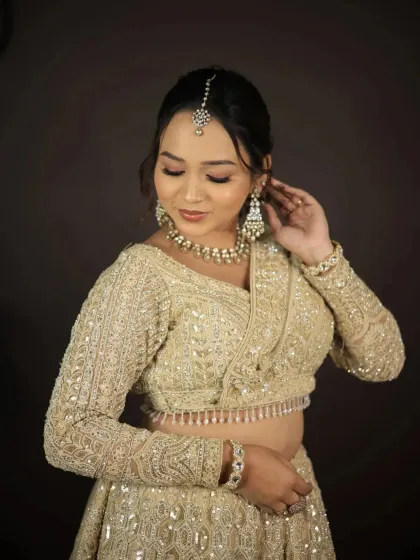 A close-up of a model in a golden-beige lehenga, adjusting her earring.