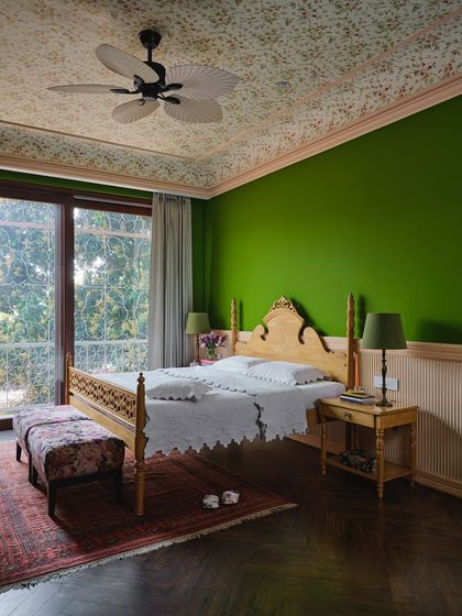 Wrapped in forest green, the artist's bedroom is designed like a canvas. A floral wallpapered ceiling, ash-pink paneling, and a refurbished four-poster bed create a space that is vibrant and imaginative.