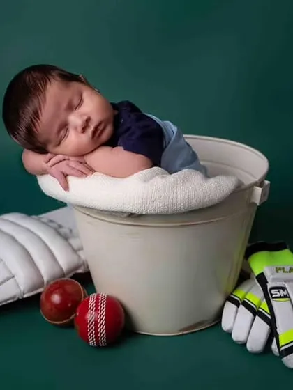 Dreaming of a century! This newborn is posed as a future cricket star, complete with a miniature bat, ball, and pads. A perfect theme for a cricket-loving family.