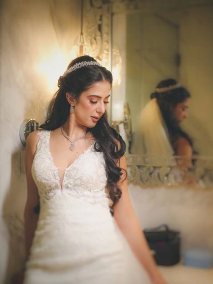 A bride getting ready in a white wedding gown, her reflection visible in the mirror.
